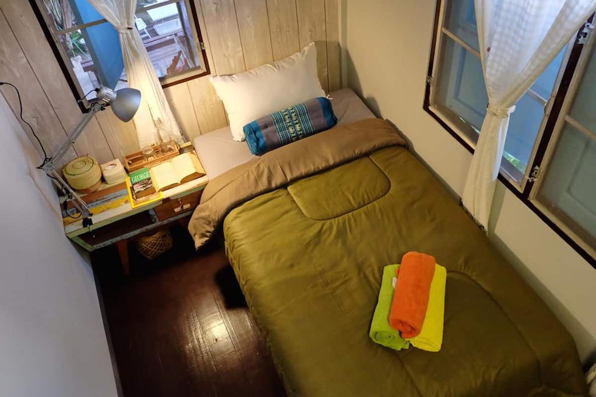 Une petite pièce agréable, avec un lit, un bureau doté d’une lampe et une fenêtre avec des rideaux.
