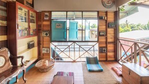 A cozy room with wooden walls, a large window with blue shutters, a wooden cabinet, and a small table with a cushion. - Sor Vorapin Muay Thai Home (Bangkok)
