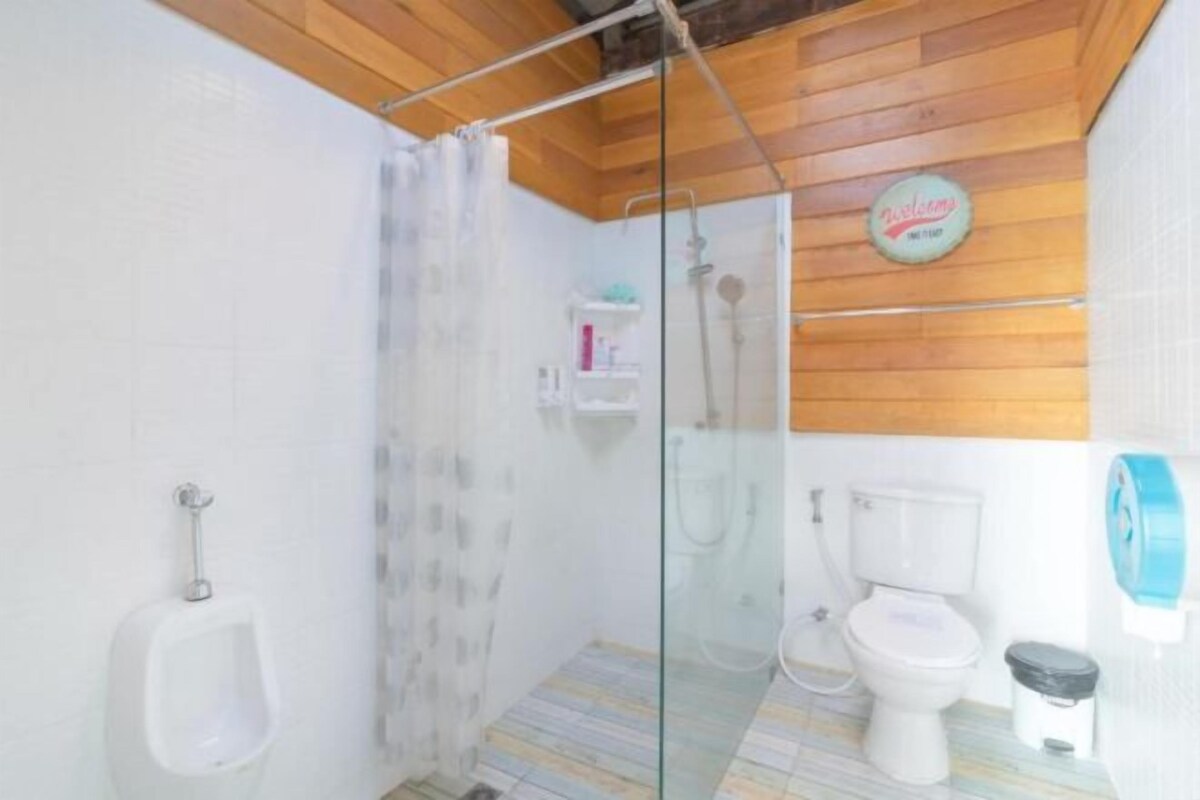 Une salle de bain équipée d’une douche à parois de verre, d’un urinoir, de toilettes et d’un distributeur de savon.