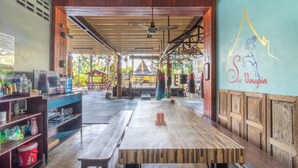 A spacious indoor area with a wooden table and benches, a punching bag, and a wall with a logo. - Sor Vorapin Muay Thai Home (Bangkok)