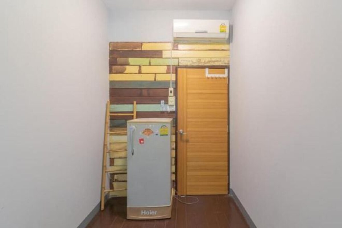 Een compacte kamer met een kleine koelkast, een houten deur en een muur met een decoratief patroon.