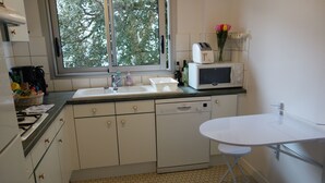 A kitchen with white cabinets, a sink, a dishwasher, a microwave, and a small table. - T3 - Quartier Le Parc 200 m from the beach, parking, elevator, terrace, shops (Royan)