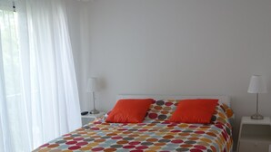A bedroom with a bed, white curtains, a ceiling light, and a nightstand with a lamp. - T3 - Quartier Le Parc 200 m from the beach, parking, elevator, terrace, shops (Royan)