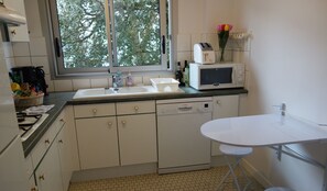 Una cocina con armarios blancos, un lavabo, lavavajillas, microondas y una pequeña mesa.