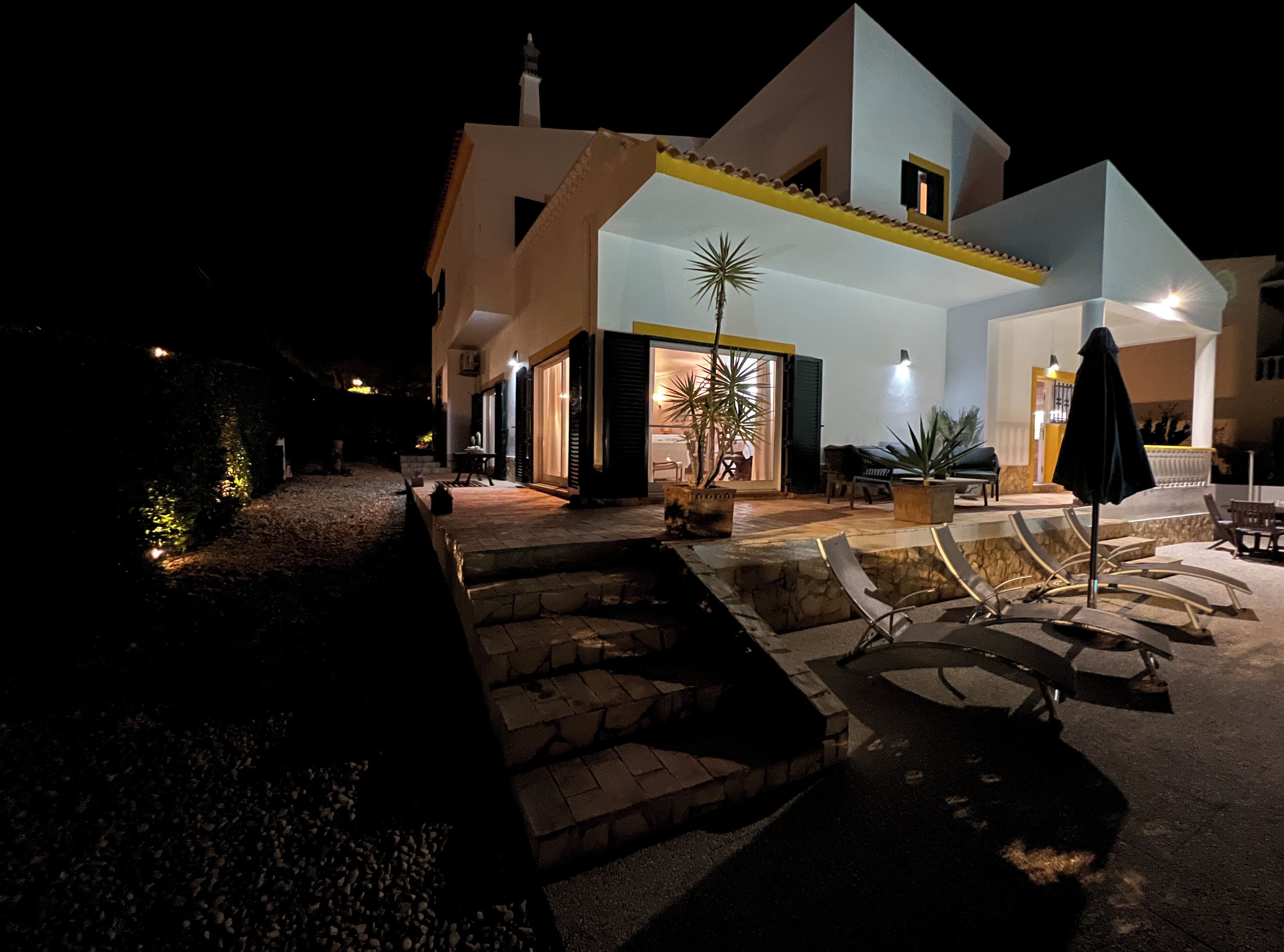 Una casa de dos pisos con un patio, mobiliario exterior y macetas con plantas.