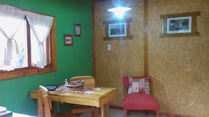 A dining area with a wooden table, chairs, and a red cushioned bench. There are framed pictures on the wall and a window with curtains. - Tierras del Sur I (Villa La Angostura)