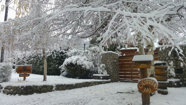 A snow-covered entrance with stone walls and wooden gates, signs indicating 'Acuerpar por dia' and 'Caminito 340'. - Tierras del Sur I (Villa La Angostura)