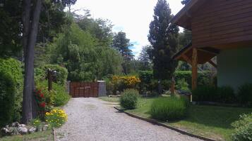 Uma entrada de cascalho leva a um portão de madeira, cercada por vegetação exuberante e árvores.