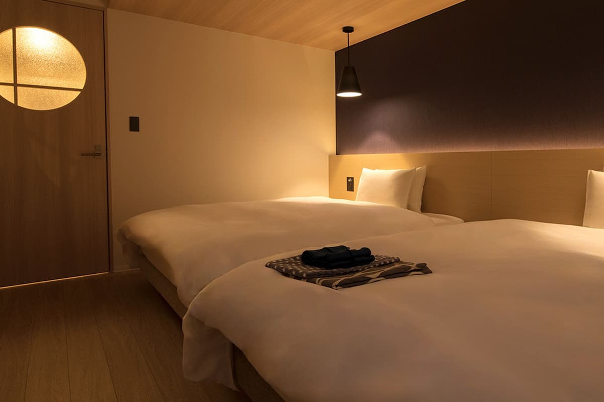 Habitación de hotel con dos camas, un ventanal redondo, una pared oscura y una lámpara colgante.