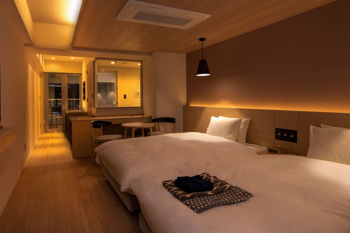 Habitación de hotel con una cama grande, mesitas de noche, un espejo y un pequeño rincón de descanso con una mesa y sillas.