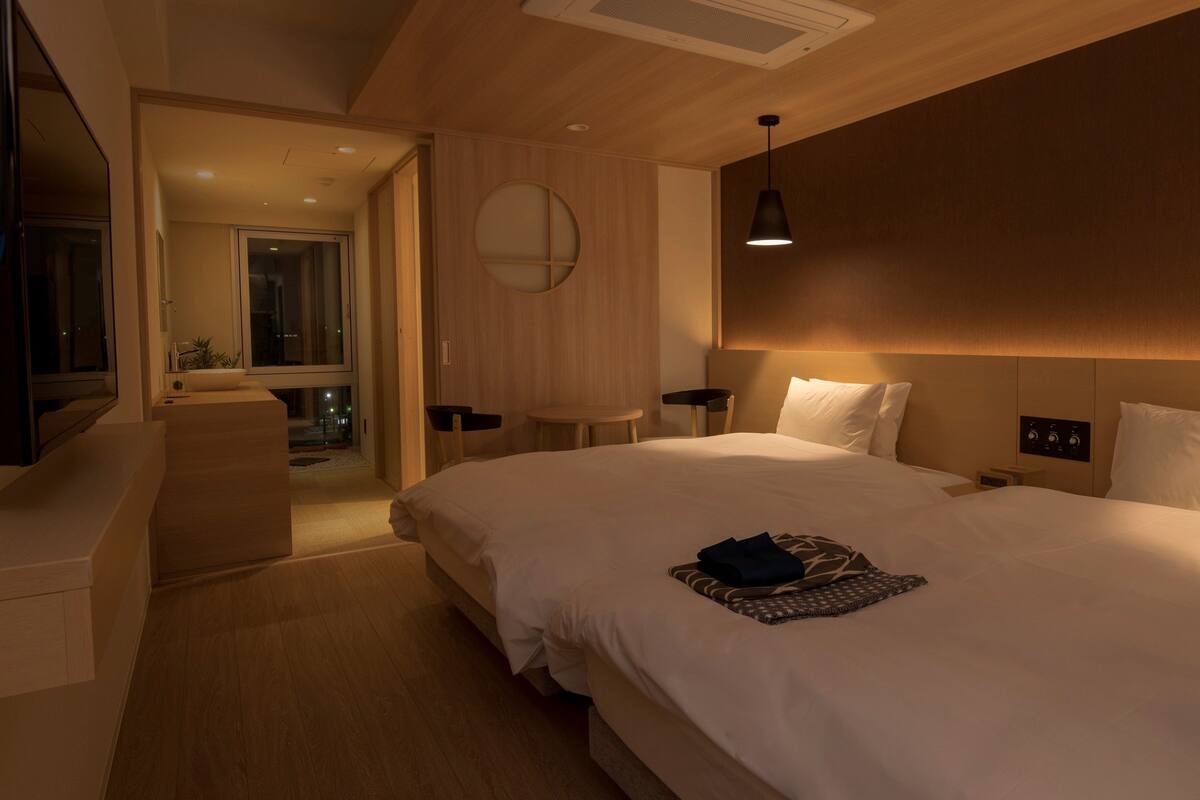 Habitación de hotel moderna con una cama grande, mesitas de noche, televisor y vistas a la ciudad de noche.