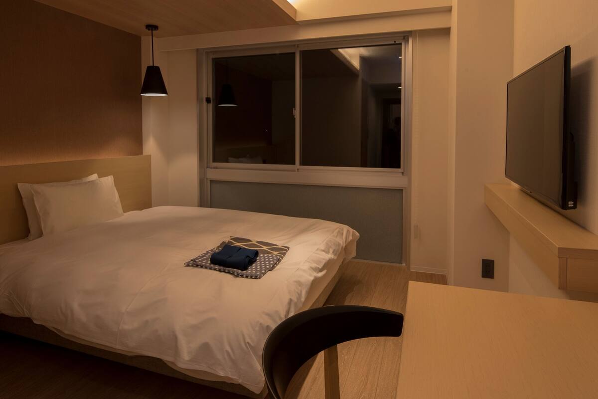 Una habitación de hotel con cama, escritorio, silla, televisor y ventana.