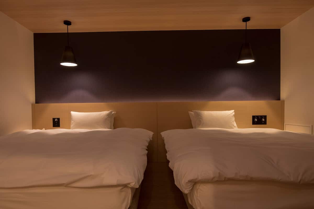 Habitación de hotel con dos camas, cada una con cabecera y controles junto a la cama.