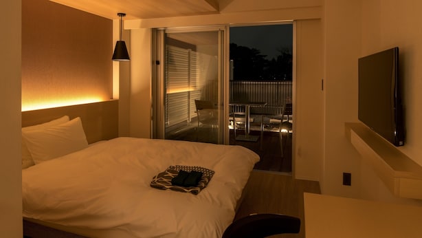 A hotel room with a bed, a TV, a chair, and a balcony with a table and chairs.