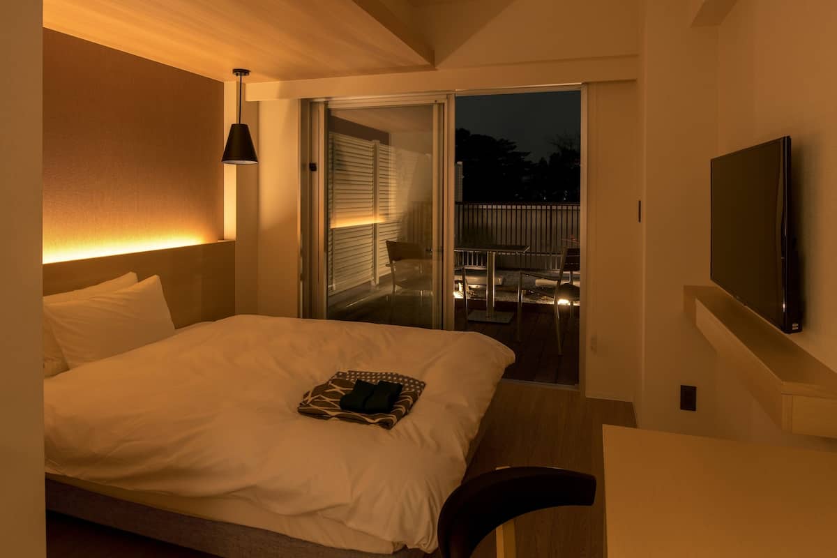 Habitación de hotel con cama, televisión, sillón y balcón con mesa y sillas.