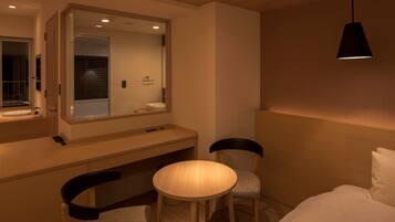A modern hotel room with a large mirror, a round table, two chairs, a bed, and a hanging light fixture.