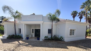 Una casa moderna con entrada pavimentada, fachada blanca y palmeras.
