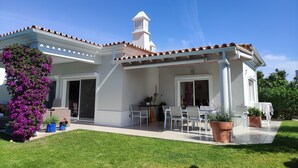 Una casa con porche cubierto, fachada blanca y tejado de tejas rojas.