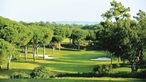 Campo de golf con árboles, un búnker de arena y cielo despejado.