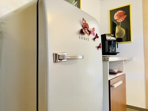 Eine Küche mit einem weißen Bosch-Kühlschrank, einer Kaffeemaschine und einem Bild an der Wand.