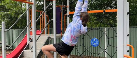 A child climbing monkey bars at a playground with a red slide and a spider-themed sign.