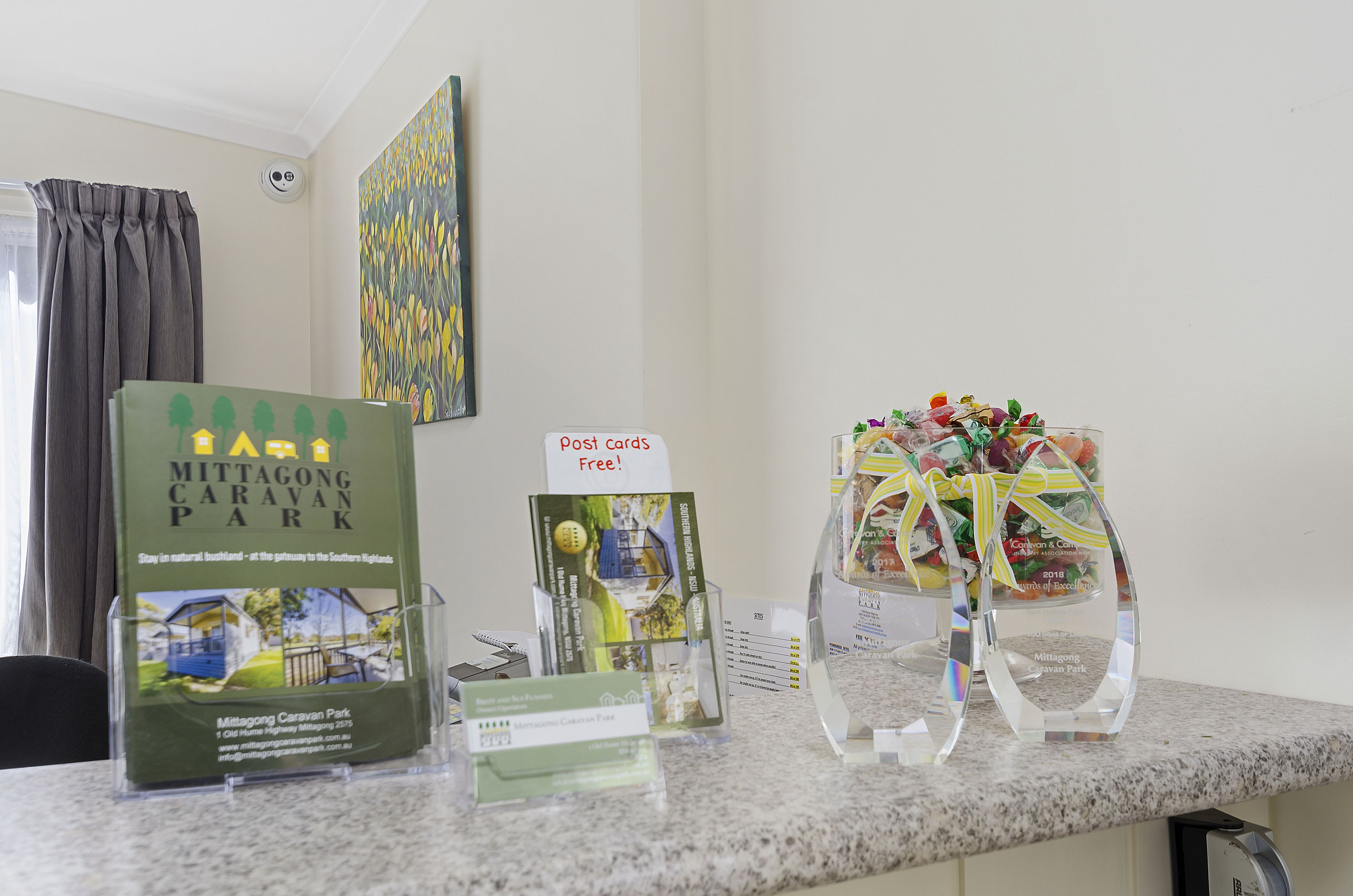 A counter with promotional materials for Mititgong Caravan Park, including postcards and a glass display with a ribbon.