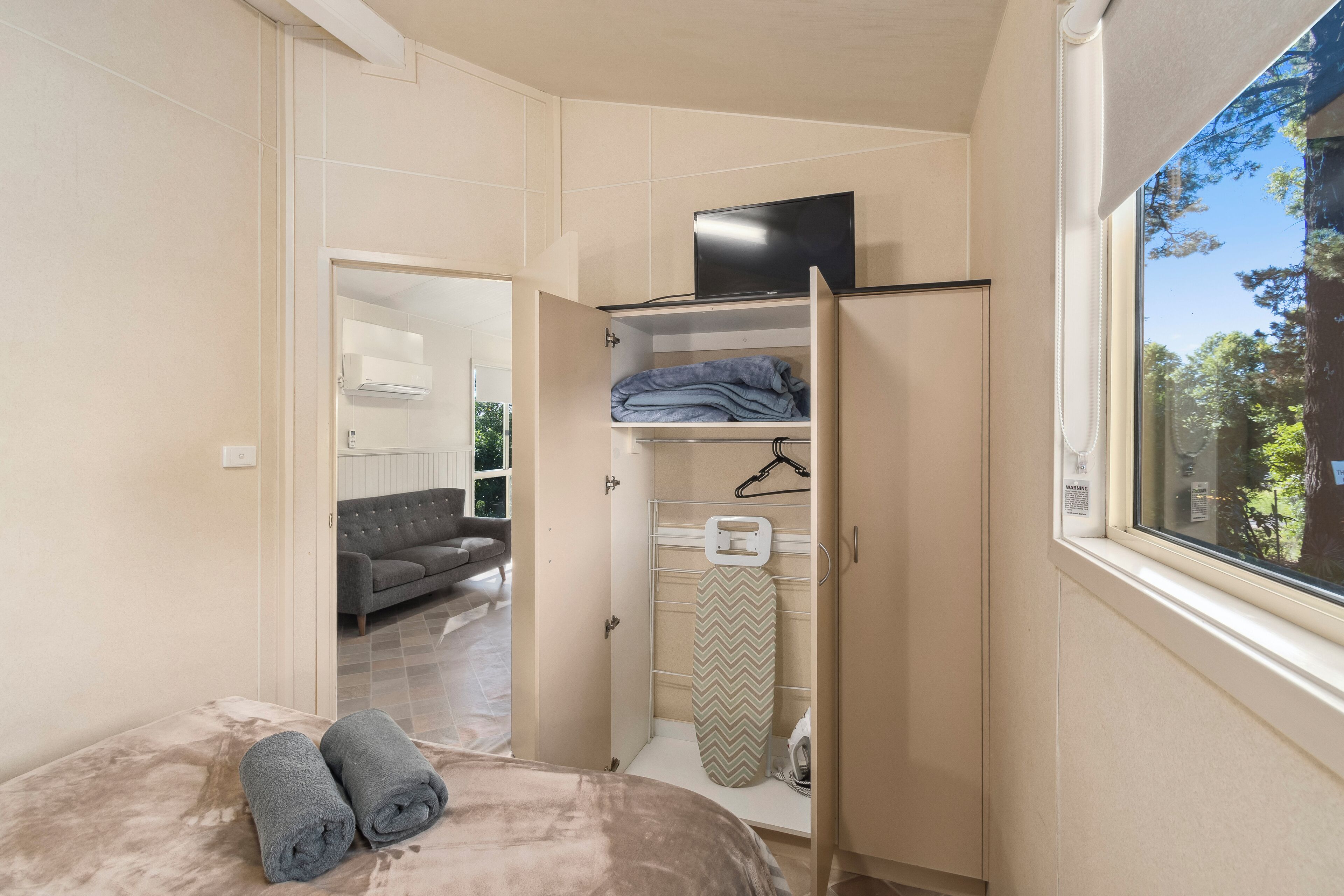 Un dormitorio con cama, armario, televisor y ventana con vistas a árboles.