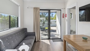 Una sala moderna con un sofá gris, una mesa de comedor de madera y un ventanal corredero que da a un patio exterior.