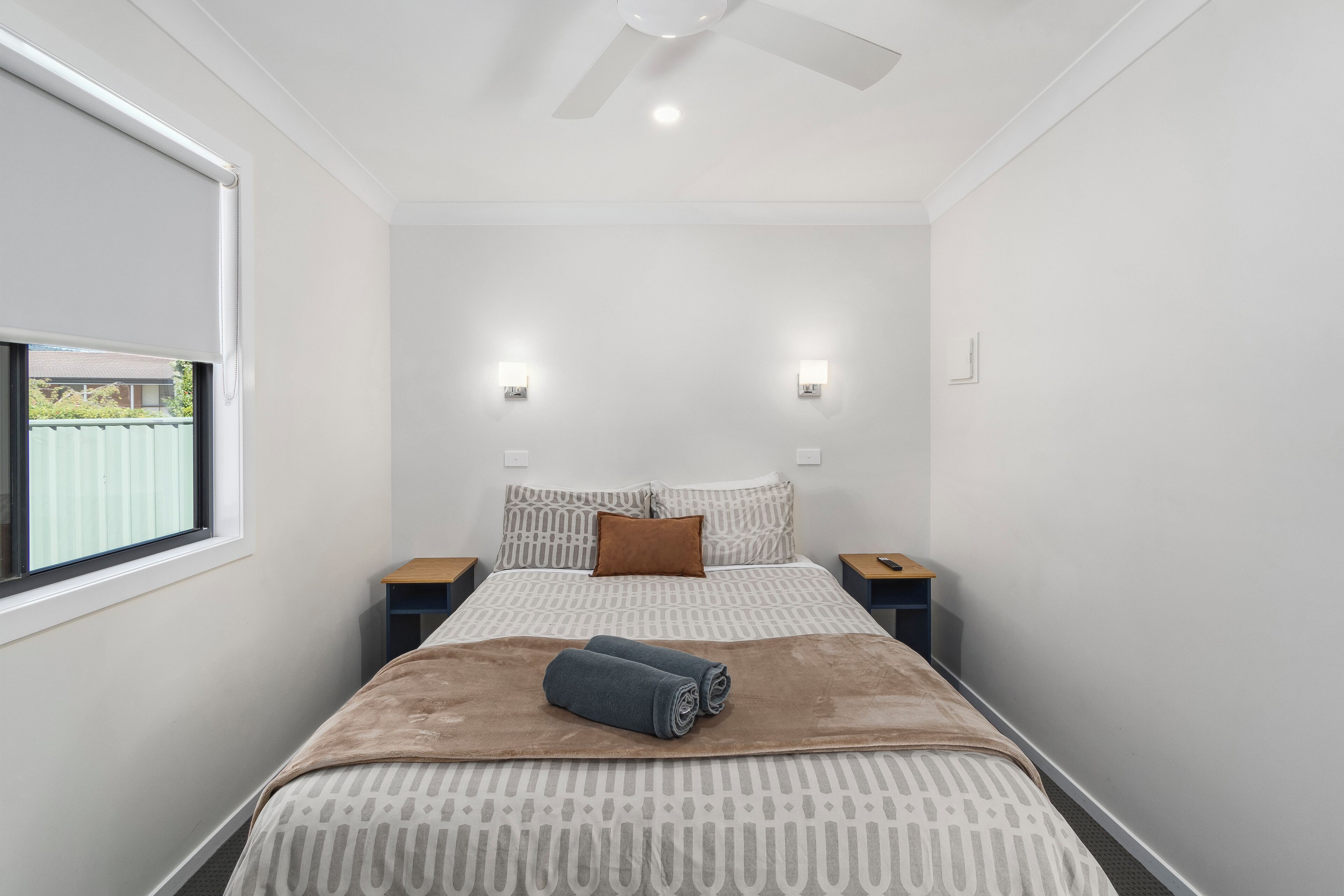 Un dormitorio con una cama, dos mesitas de noche, un ventilador de techo y una ventana.
