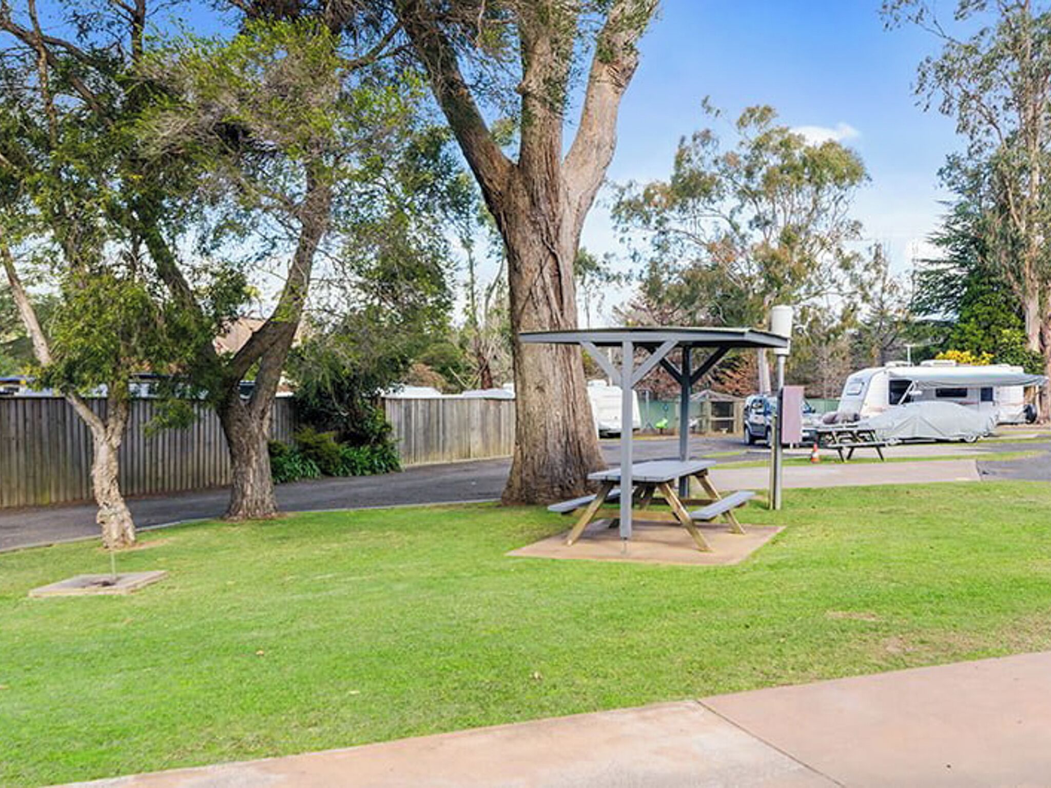 A picnic area with a metal shelter and benches, surrounded by trees and a grassy field.
