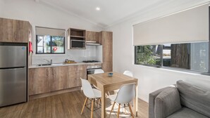 Una cocina moderna con armarios de madera, un refrigerador de acero inoxidable, un microondas y un comedor con una mesa de madera y sillas blancas.