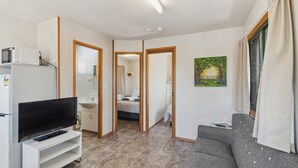 Un espacio habitable compacto con televisor de pantalla plana, kitchenette y un sofá gris.