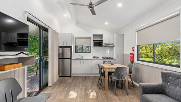 Una cocina moderna con comedor, ventilador de techo y vistas a la vegetación.