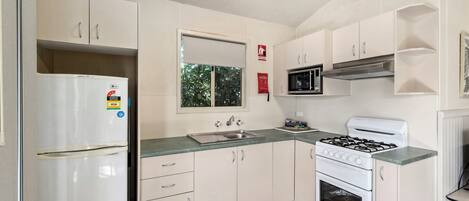 A compact kitchen with white cabinets, a stainless steel refrigerator, a microwave, a gas stove, and a sink.