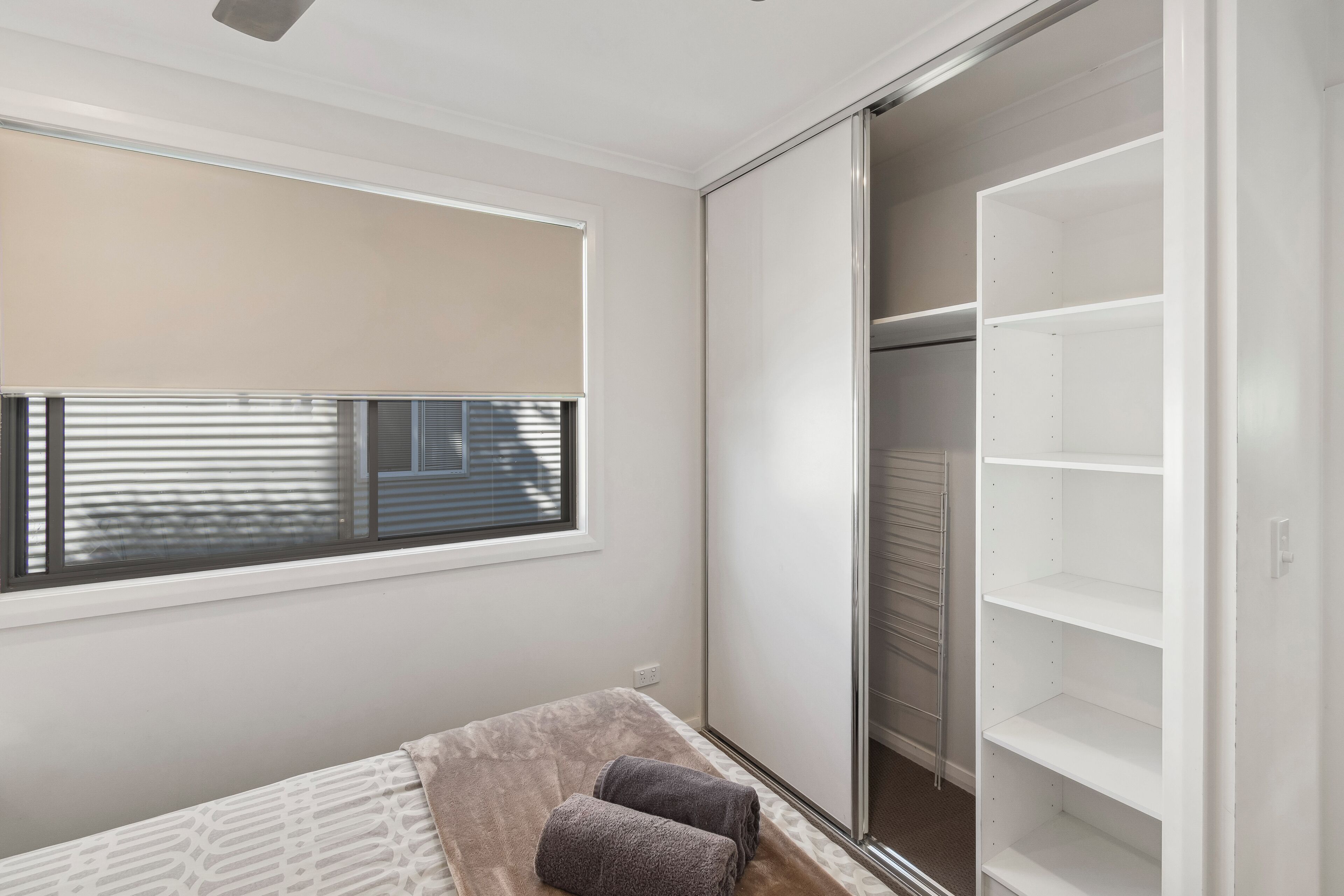 A bedroom with a bed, a window with blinds, and a closet with shelves.