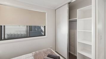 A bedroom with a bed, a window with blinds, and a closet with shelves.