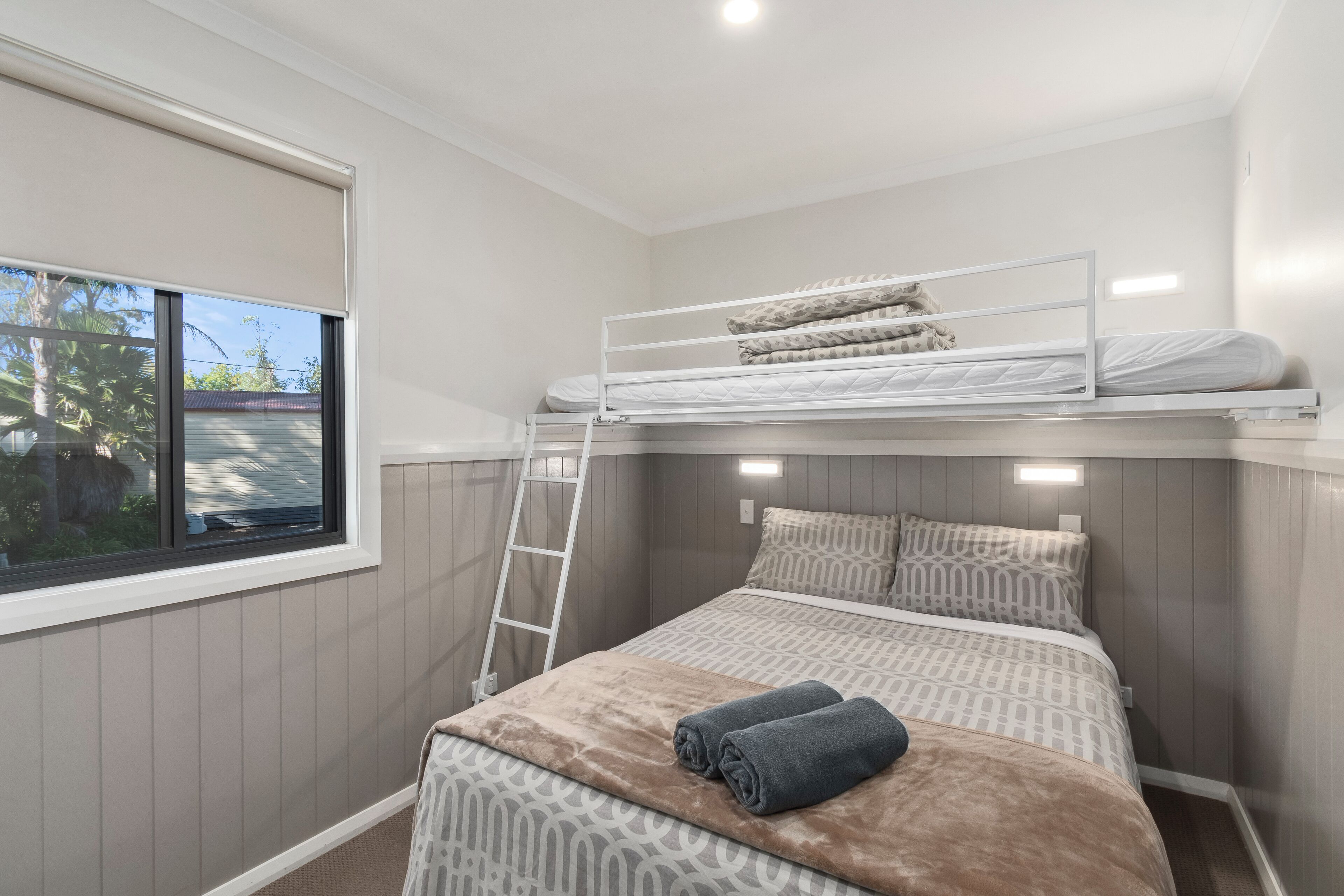 Habitació amb literes, una finestra, una escala i un edredó amb motius.