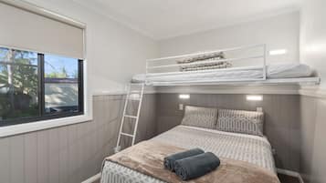 Habitació amb literes, una finestra, una escala i un edredó amb motius.