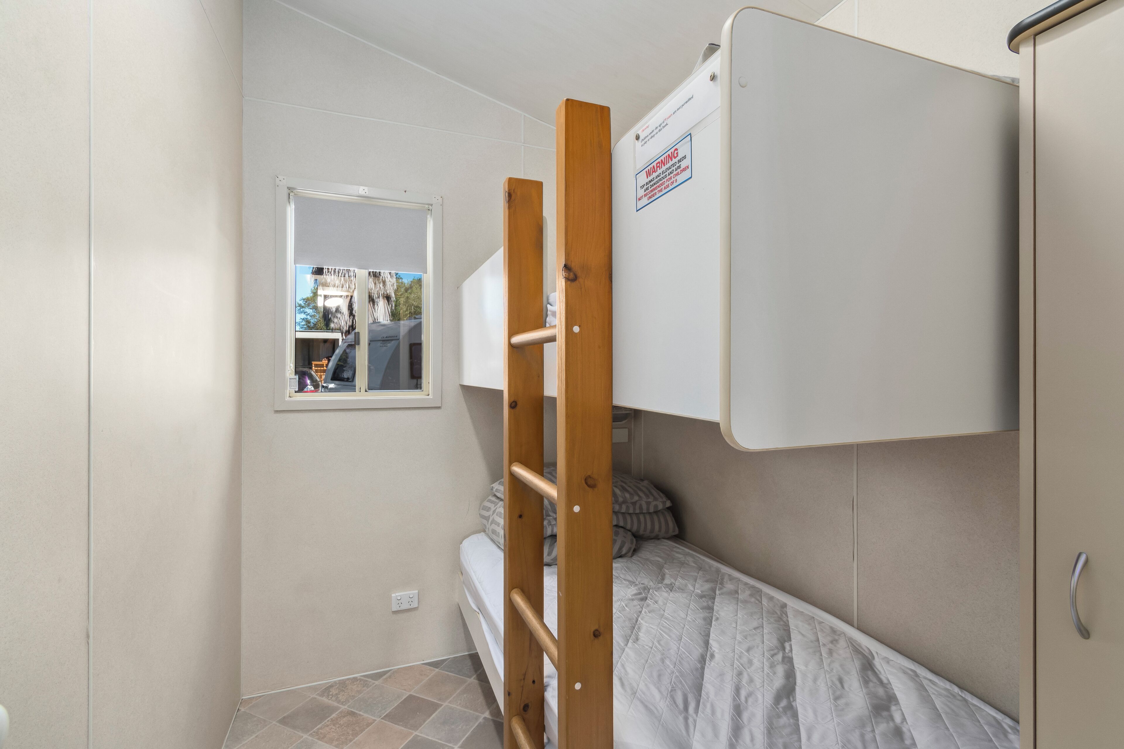 Una stanza piccola e compatta con un letto a castello, una scala in legno, una finestra e una porta.