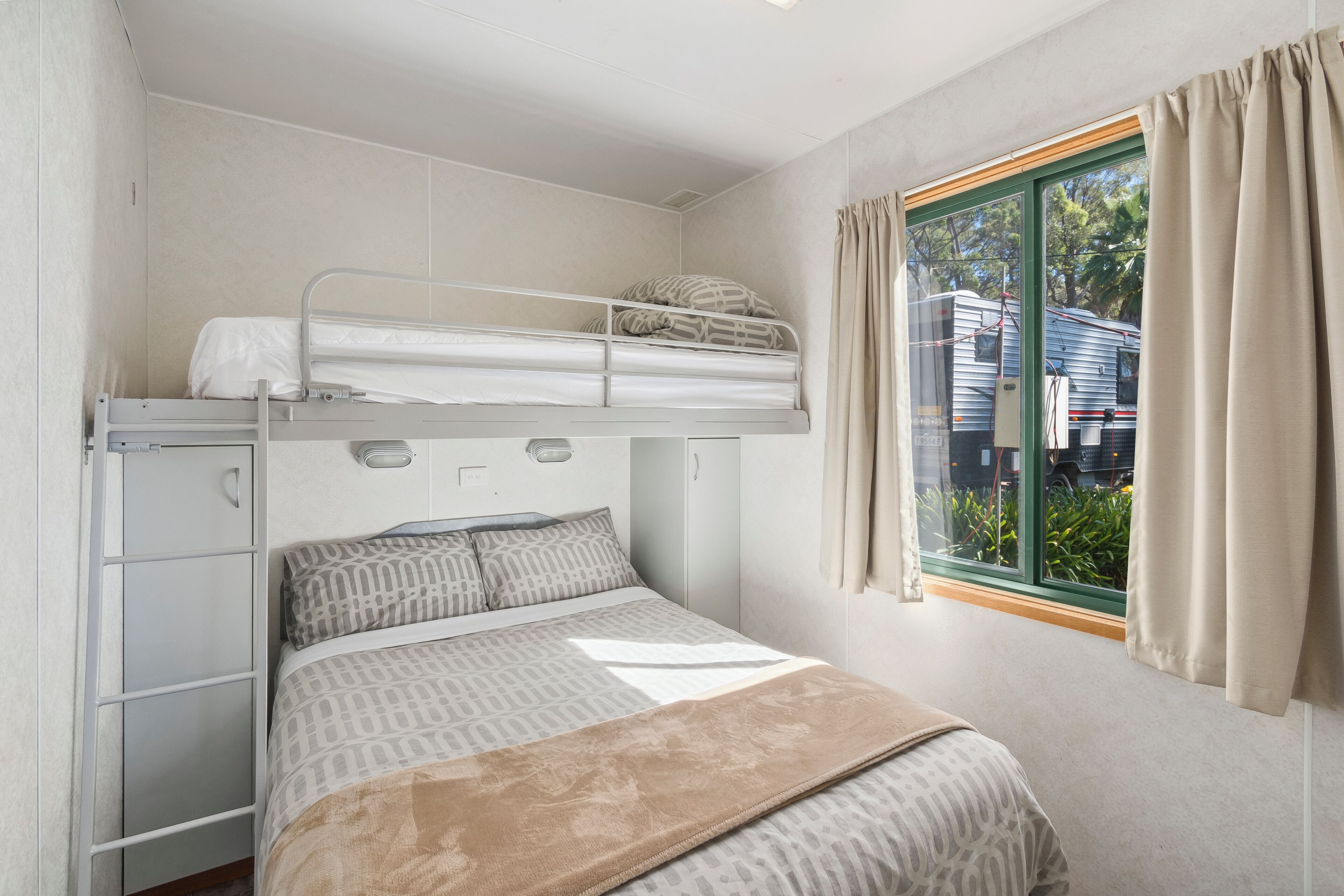 Quarto com beliche, janela, cortinas e vista para uma casa lá fora.