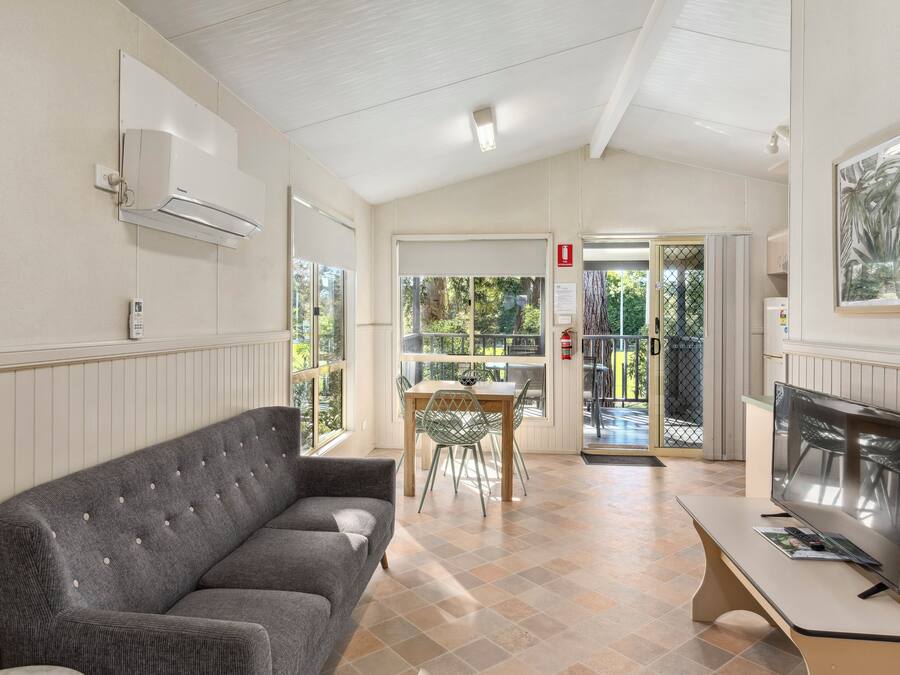 A room with a grey sofa, a TV on a stand, a dining table with chairs, and a door leading outside.