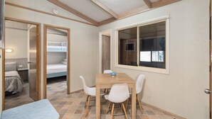 Una habitación con una mesa de madera, sillas blancas, una cama litera y una ventana con persianas.