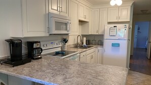 A kitchen with white cabinets, a microwave, a refrigerator, a stove, and a coffee maker.