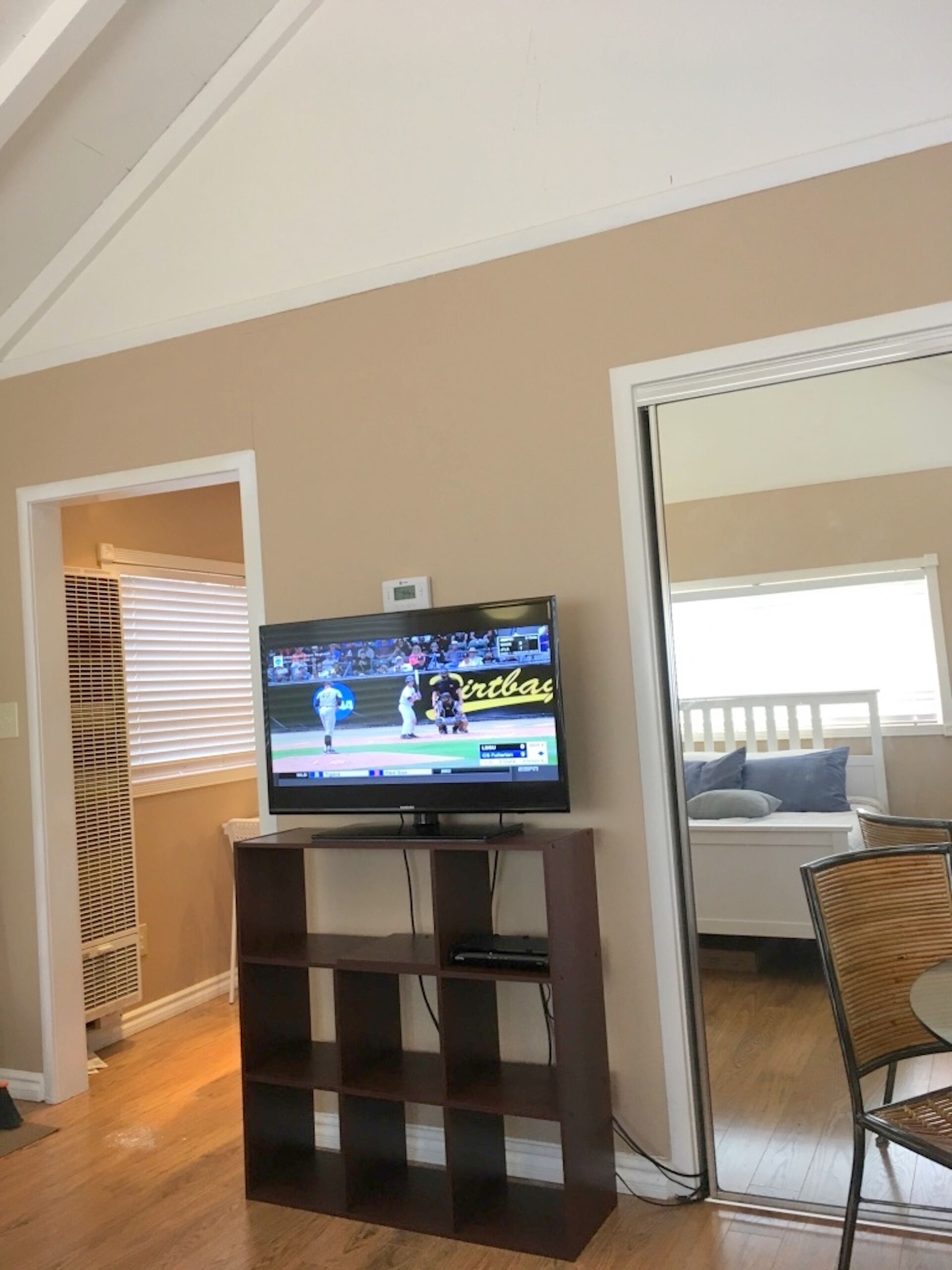 A living room with a flat-screen TV on a wooden stand, a white couch, and a wicker chair.