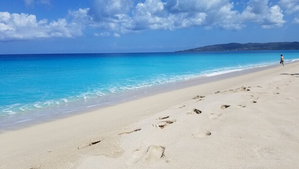 A beach with clear turquoise water, a sandy shore, and footprints leading into the water. - Escape to the Caribbean! Beachfront Condo Starting at Just $145/Night! (Christiansted)