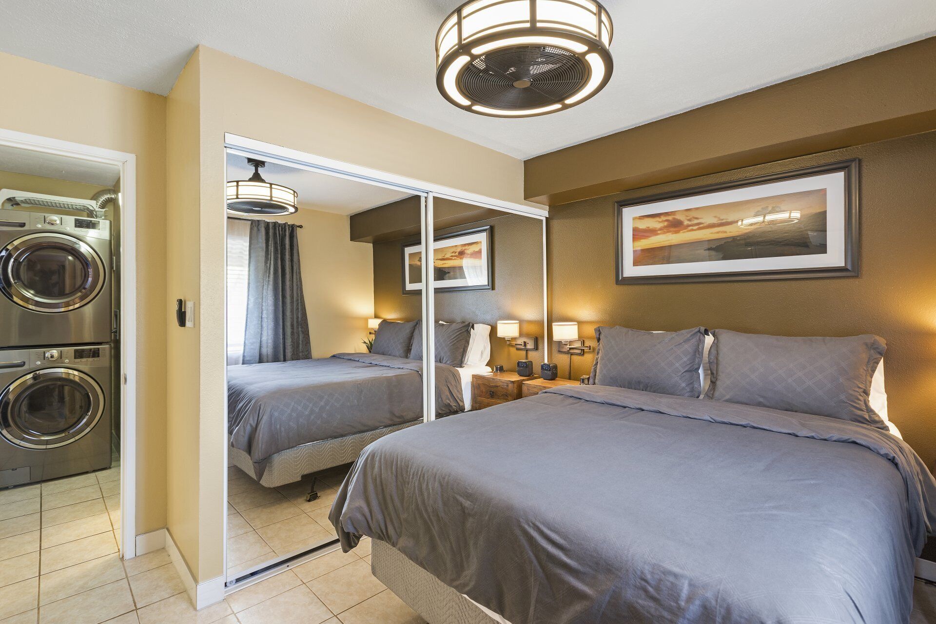 A hotel room with two beds, a washing machine, a mirror, and a ceiling fan.