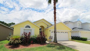 A yellow single-story house with a garage, surrounded by well-maintained lawn and tropical plants.