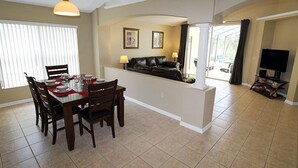 A dining area with a table set for four, a black leather sofa, and a television in the corner.