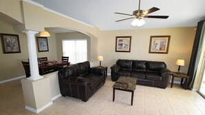 A spacious living room with a dining area, a ceiling fan, and artwork on the walls.