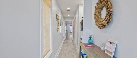 A hallway with a wooden floor, a wall-mounted mirror, and a bulletin board with papers.